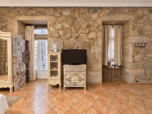 Loft en Baiona con paredes de piedra vista, suelos de madera, mobiliario color crema, televisión y ventanas con vistas a la ciudad