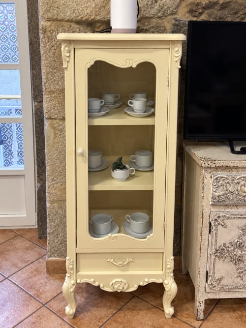 Mueble crema con puerta de cristal exhibiendo vajilla en apartamento de Baiona