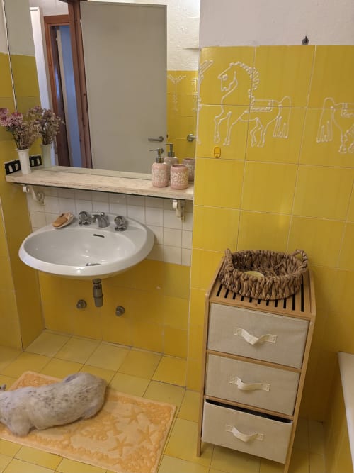 Bagno luminoso con piastrelle giallo brillante presso Chickens' Maisons Porto Cervo, con lavabo rotondo, specchio e cesto in vimini