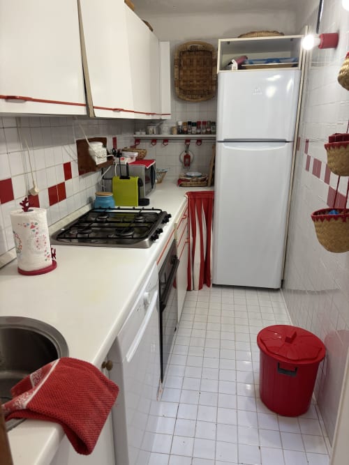 Compatta cucina a galera nell'appartamento di Porto Cervo con arredamento rosso e bianco, fornello a gas, frigorifero e pavimenti piastrellati.