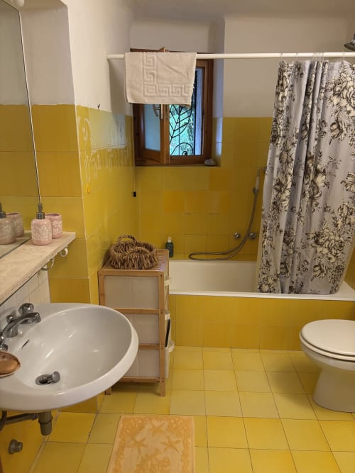 Bagno giallo luminoso con lavabo rotondo, toilette, doccia e finestra nell'appartamento Chickens' Maisons a Porto Cervo, Italia