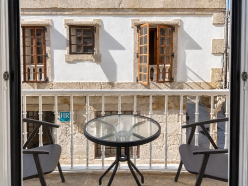 Balcón de Baiona con dos sillas y mesa redonda con vistas a edificio histórico de piedra con puertas y ventanas de madera