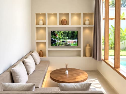 Elegante sala de estar de villa moderna con pared de TV, sofá beige, mesa de madera redonda y vistas al jardín en Oasis Dune Villas, Lombok