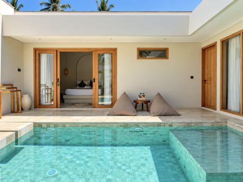 Villa de lujo con piscina turquesa, puertas de madera, zona de descanso con cojines y palmeras en Oasis Dune Villas, Lombok