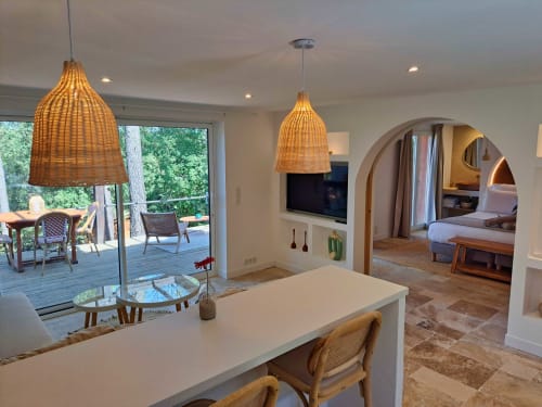 Suite Le Lodge aux Terrasses de Lorgues avec cuisine ouverte, luminaires suspendus tressés, téléviseur, passage voûté vers la chambre et jardin