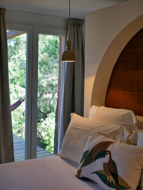 Chambre moderne aux Terrasses de Lorgues avec literie blanche, tête de lit arquée, luminaire suspendu et vue sur le jardin