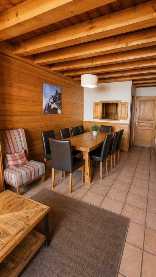 Salle à manger chaleureuse en bois avec table, chaises noires, cheminée et art montagnard au Chalet des Cimes, Belle Plagne