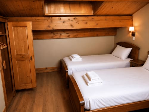 Chambre douillette en bois avec deux lits jumeaux, draps blancs et poutres rustiques au Chalet des Cimes, Belle Plagne