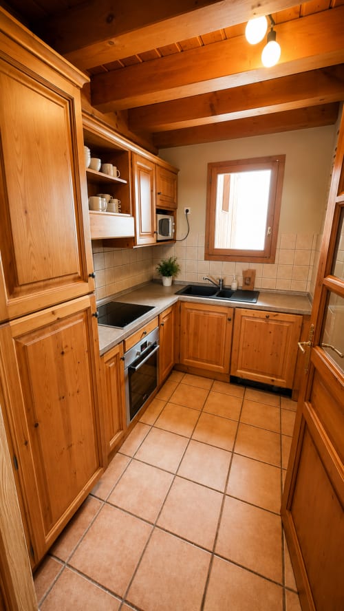 Cuisine en bois avec carrelage en terre cuite, électroménagers en acier inoxydable et poutres apparentes à l'appartement Le Chalet des Cimes