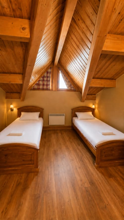 Chambre cosy mansardée du Chalet des Cimes avec deux lits jumeaux, poutres en bois, lucarne et vue sur la montagne