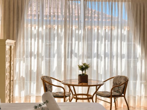 Moderno apartamento en Baiona con mesa redonda de madera, dos sillas y cortinas translúcidas del piso al techo que filtran la luz natural