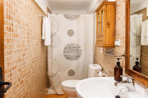 Modern bathroom in Chulilla apartment with brick walls, white sink, toilet, and shower with geometric curtain