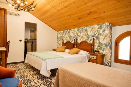 Spacious triple room at Serranía hotel in Chulilla with wooden beamed ceiling, garden view wallpaper, and comfortable