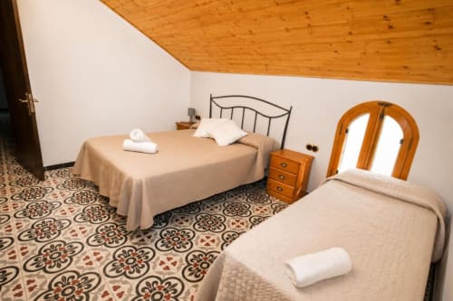 Triple bedroom in Chulilla hotel with two beds, wooden ceiling, patterned tile floor, and arched doorway window.