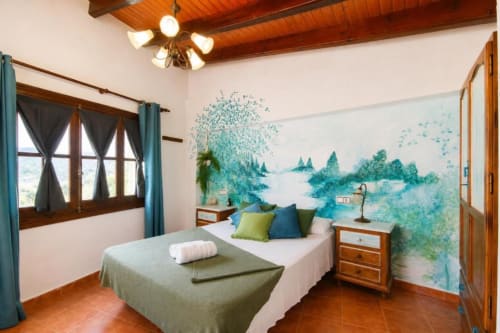 Serranía double room with turquoise landscape mural, wooden beams, garden view window, and terracotta floors in Chulilla