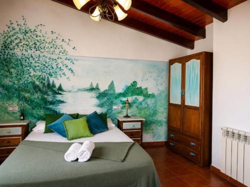 Serranía double bedroom with scenic lake mural, wooden beams, green bedding, and garden views