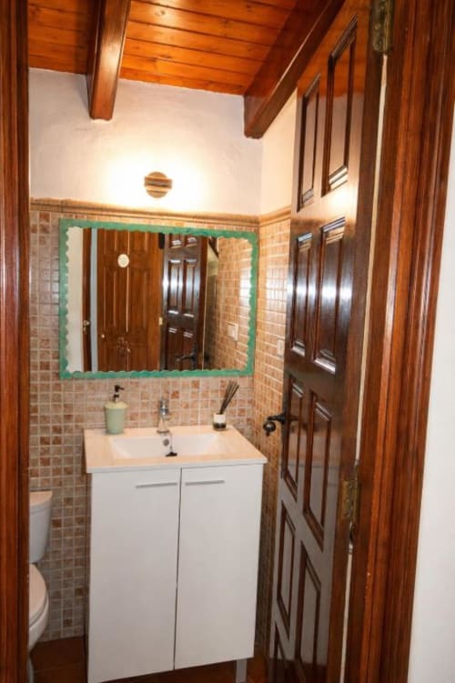 Modern bathroom in Chulilla hotel with white vanity, turquoise-framed mirror, tile walls, and wooden beams