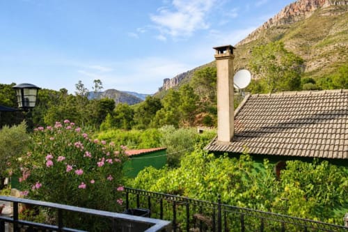 Mountain garden view of Chulilla apartment with pink flowers, tiled roof, and olive trees