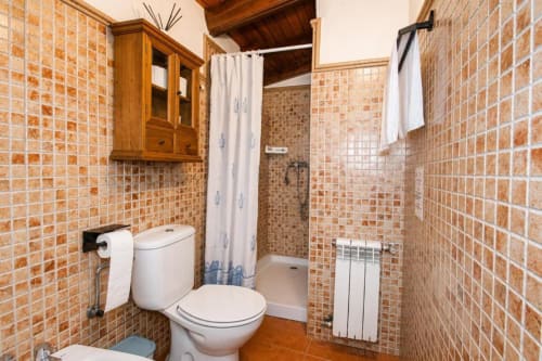 Rustic bathroom at Serranía Gestión hotel in Chulilla with terracotta tiling, toilet, shower, and wooden storage cabinet