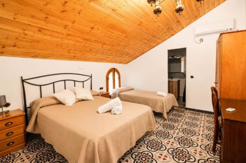 Triple room at Serranía hotel in Chulilla with two beds, wooden ceiling, and patterned tile floor