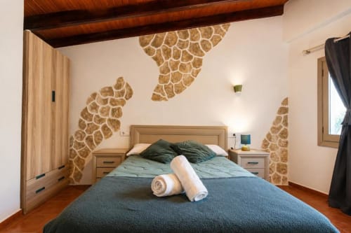 Cozy triple bedroom in Chulilla with giraffe-pattern wall art, wooden beams, and folded towels on the bed