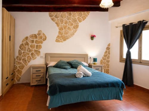 Triple room at Serranía hotel in Chulilla featuring terracotta floors, blue bedding, stone wall art, and modern amenities