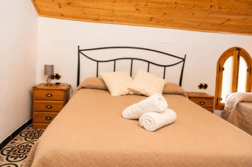 Cozy triple bedroom in Chulilla hotel with beige bedding, wrought iron headboard, wooden nightstands, and white rolled towels