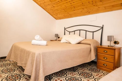 Spacious triple room at Serranía hotel in Chulilla with wrought iron bed, wooden ceiling, and patterned tile floors
