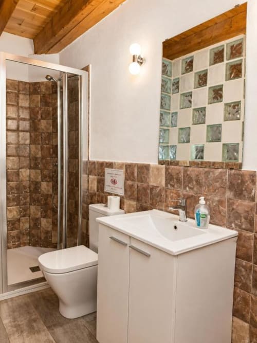 Modern bathroom with brown tiled walls, white sink vanity, toilet, and glass shower enclosure in Chulilla hotel room
