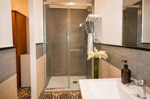 Modern bathroom with glass shower enclosure, white sink, and decorative tile flooring at Serranía hotel in Chulilla
