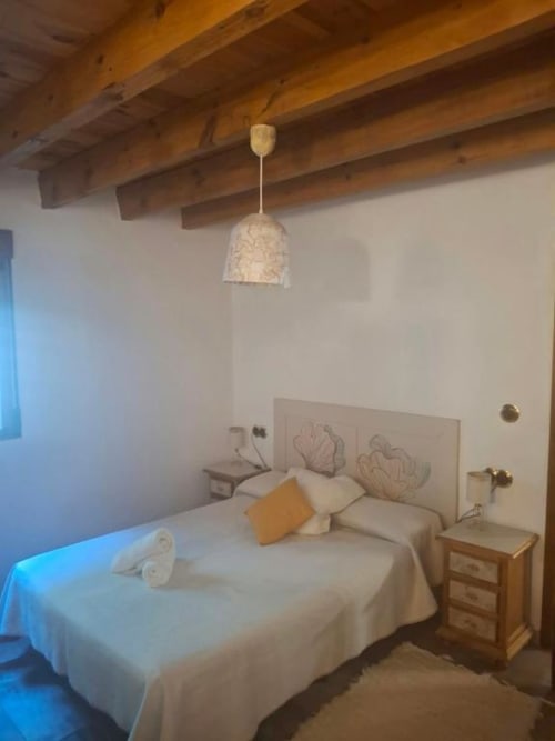 Modern triple bedroom in Chulilla with wooden beams, cream bedding, rustic nightstand, and pendant lighting