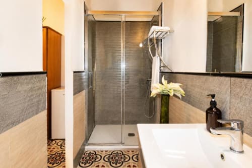 Modern bathroom in Chulilla with walk-in shower, white sink, decorative tile flooring, and green flower arrangement