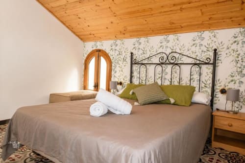 Cozy double bedroom at Serranía hotel in Chulilla with wrought iron bed, green pillows, wooden ceiling, and botanical
