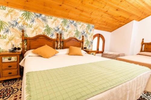 Bright triple room at Serranía hotel in Chulilla with wooden furnishings, garden wallpaper, and green bedding