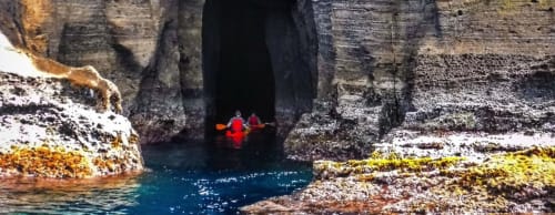 Red kayak entering coastal cave at Golden Mermaid Villa, Ribeirinha Portugal with turquoise water