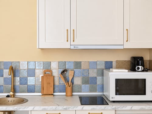 Cocina moderna en apartamento de Baiona con azulejos azules, encimera de mármol, armarios blancos y acero inoxidable