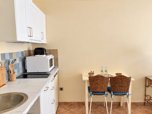 Moderna cocina americana en Baiona con muebles blancos, microondas, mesa de comedor y sillas de mimbre