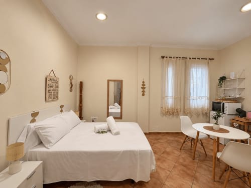 Luminosa habitación en Holibai Baiona con cama blanca, escritorio moderno, cocina americana y suelo de madera en apartamento privado