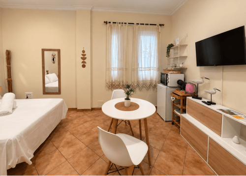 Apartamento Holibai en Baiona con cama, mesa redonda blanca, TV, cocina americana y mobiliario moderno en tonos cálidos.