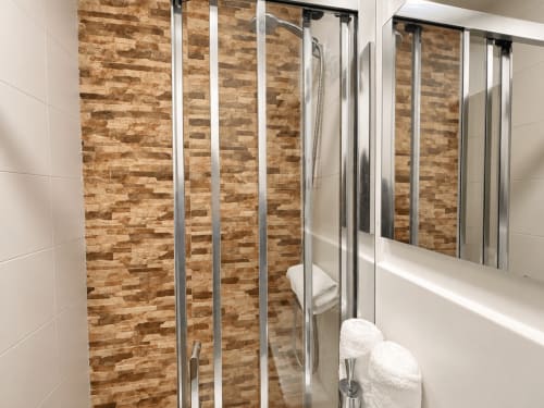 Baño moderno en apartamento Holibai con pared de ladrillo visto, ducha de cristal, azulejos blancos y toallas