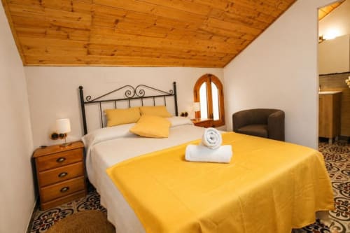 Bright bedroom at Serranía hotel in Chulilla with yellow bedding, wooden ceiling, metal bed frame, and garden views