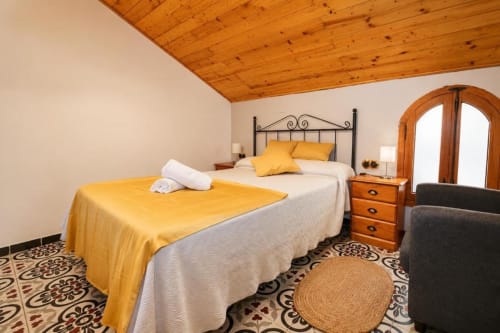 Bright bedroom with twin beds, wooden beams, wrought iron headboard, and arched doorway at Serranía hotel in Chulilla