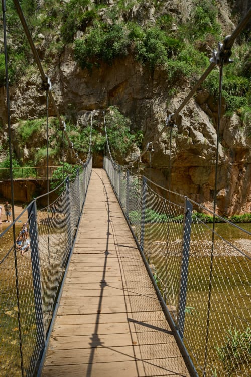 Suspended wooden footbridge crossing through rocky gorge with vegetation at Chulilla, Spain