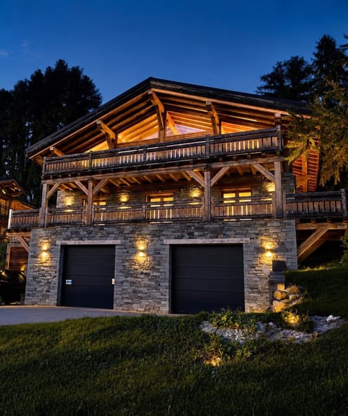 Villa Le 1611 aux Chalets d'Aline, La Plagne, illuminée au crépuscule avec balcons en bois et garage en pierre