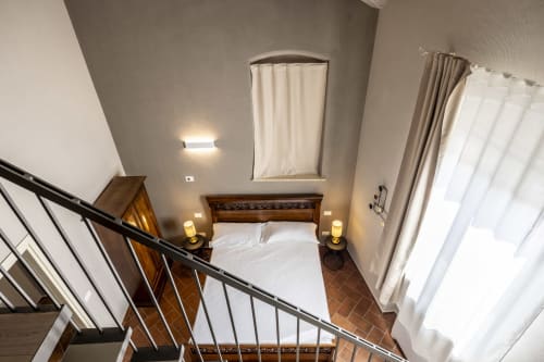 Vista elevata di una superior triple room al Corte Baruzzo Relais con vista sul giardino, letto in legno e tende color crema