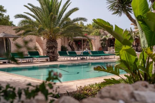 Piscine turquoise avec transats verts, palmiers et bâtiments en terre cuite à Domaine Belhazar, Essaouira