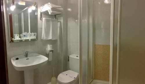 Baño del Hotel JM El Emigrante con lavamanos de pedestal, inodoro, ducha, espejo iluminado y toallero en Villanueva de la