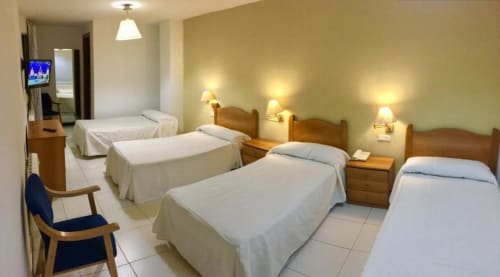 Habitación cuádruple en Hotel JM El Emigrante en Villanueva de la Serena con cuatro camas, cabeceros de madera y apliques de pared