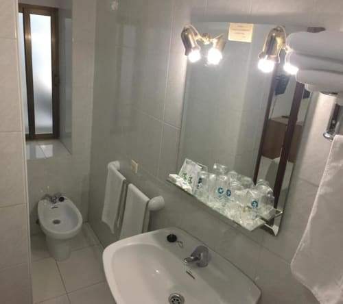 Baño del Hotel JM El Emigrante con lavabo, inodoro, espejo iluminado y artículos de tocador en Villanueva de la Serena