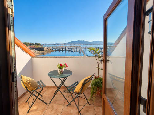 Terraza frente al mar en Baiona con dos sillas amarillas, mesita con flores, vistas a la marina y las montañas
